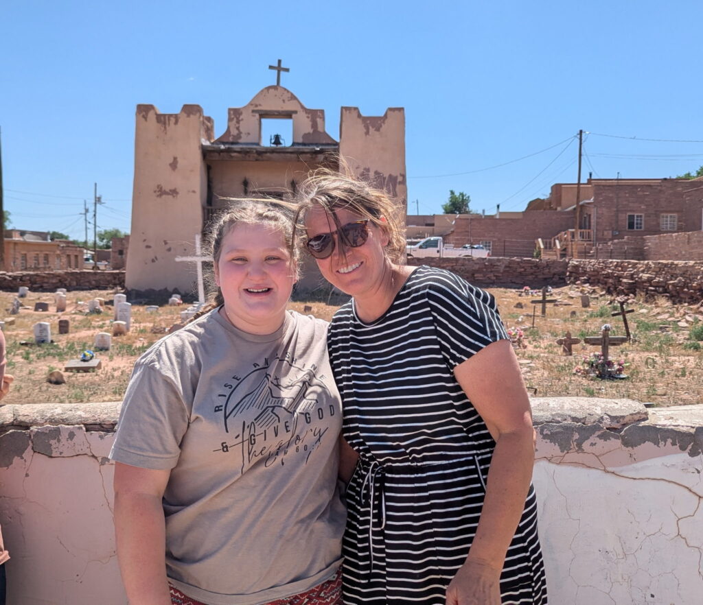 Bonnie and Missionary Amanda Herndon smiling in front of an old Southwestern church and cemetery on the Navajo Nation.